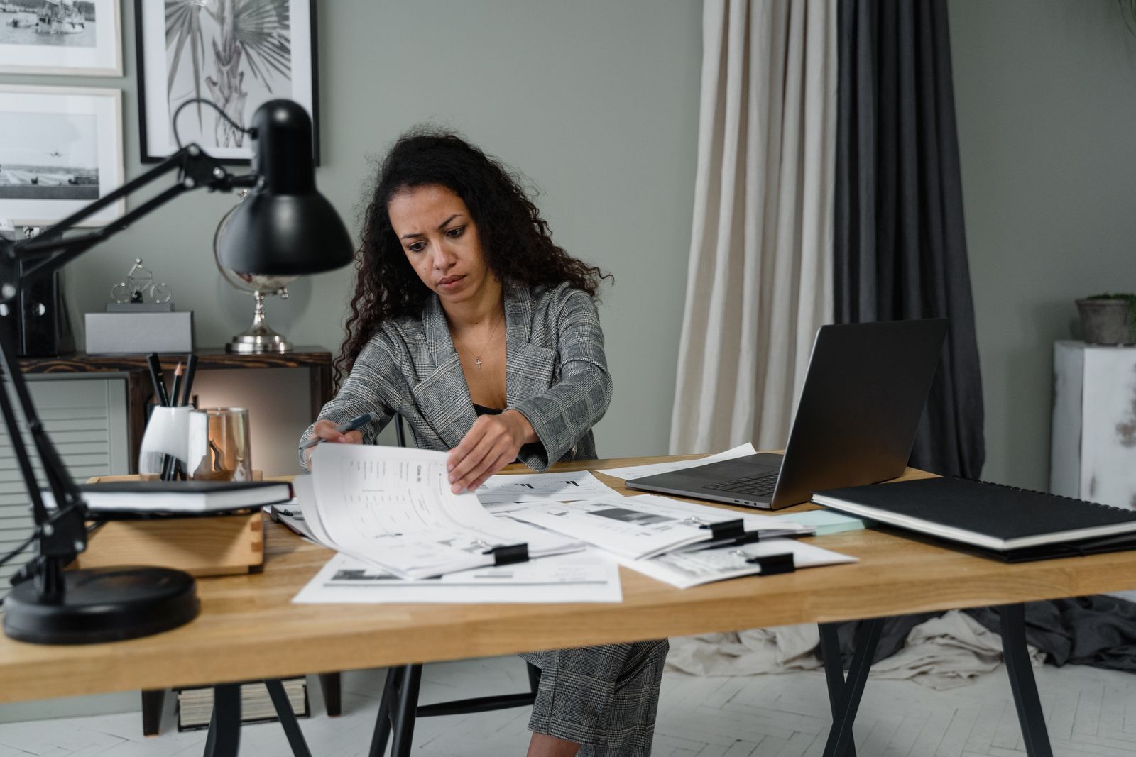 A professional reviewing printed documents beside a laptop at a window-lit desk