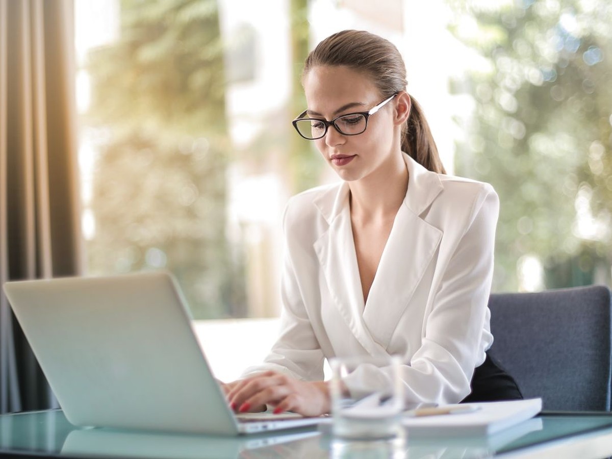 A professional in a white blazer working independently on a laptop in soft window light